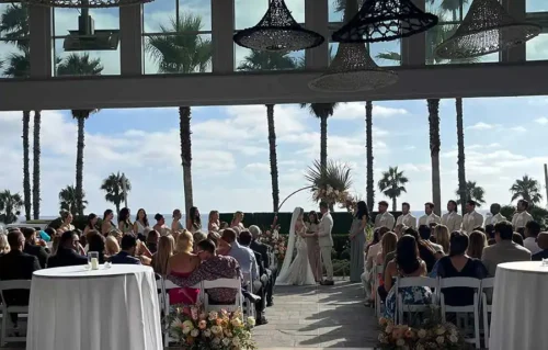 Outdoor coastal wedding ceremony with bride groom and guests under woven light fixtures in San Diego.
