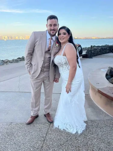 Bride and groom posing by the waterfront after their wedding ceremony in Monterey, California, with scenic coastal views in the background.