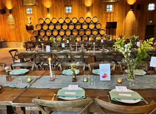 Elegant rustic barn wedding reception with long banquet tables, floral centerpieces, candles, and wine barrel décor.