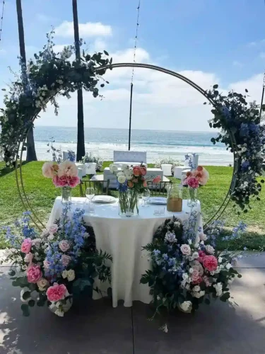 Luxury beachfront wedding sweetheart table with floral arch and ocean views in California.