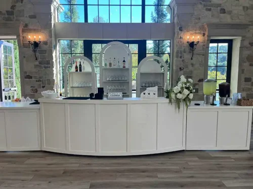 Elegant white wedding bar setup with floral arrangements, beverage dispensers, and glassware at a luxury wedding venue in San Diego, California.