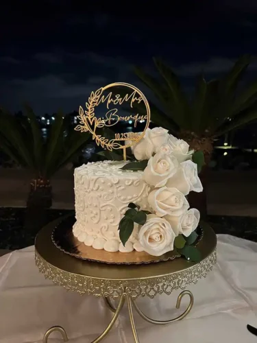 Elegant white wedding cake with handcrafted sugar roses and a personalized gold acrylic cake topper at a luxury wedding reception in Malibu, California.