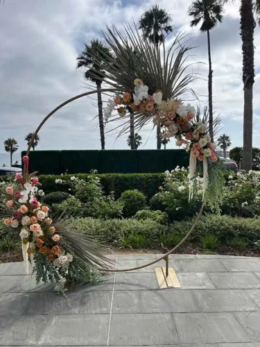Modern circular wedding ceremony arch decorated with blush and white floral arrangements and tropical greenery at a luxury outdoor wedding venue in Laguna Beach, California.