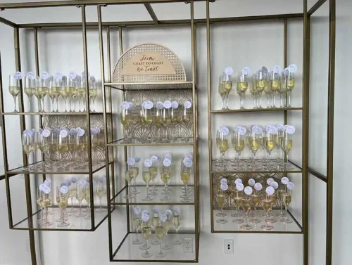 Elegant wedding champagne wall display with sparkling wine glasses on gold shelving for guests at a luxury wedding reception in Carmel-by-the-Sea, California.