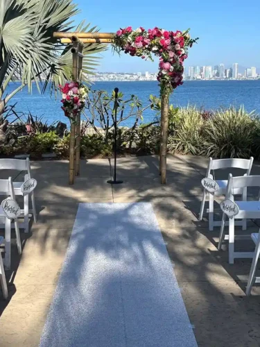 Waterfront outdoor wedding ceremony setup with a floral arch and elegant seating in California.