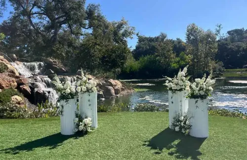 Elegant outdoor wedding ceremony setup with white floral arrangements beside a waterfall and lake in Big Sur, California.