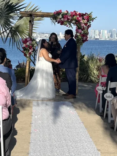 Bride and groom exchanging vows beneath a floral arch during a waterfront outdoor wedding ceremony in San Diego.
