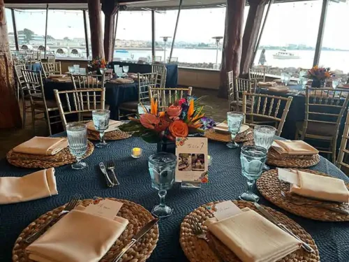 Elegant waterfront wedding reception with navy blue table linens, tropical floral centerpieces, and gold Chiavari chairs at a luxury venue in Newport Beach, California.