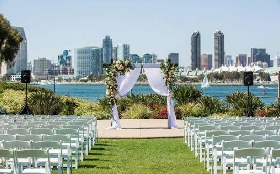 Outdoor waterfront wedding ceremony setup in Coronado, San Diego, featuring an elegant floral arch, rows of white chairs, and stunning views of the San Diego skyline across the bay.